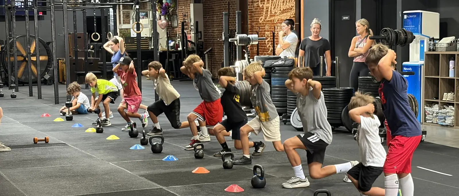Kids in a HeyKids class at Heyday Elite Fitness in San Pedro, working through a kettlebell lunge lane with coaches watching