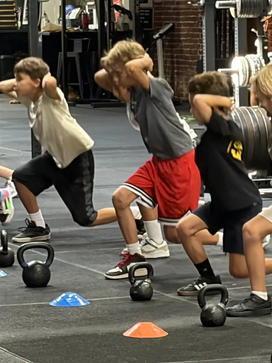 Three kids mid-lunge with kettlebells during a HeyKids class in San Pedro