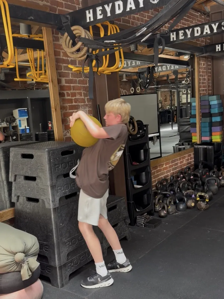 A HeyKids student carrying a medicine ball across the floor at Heyday Elite Fitness in San Pedro