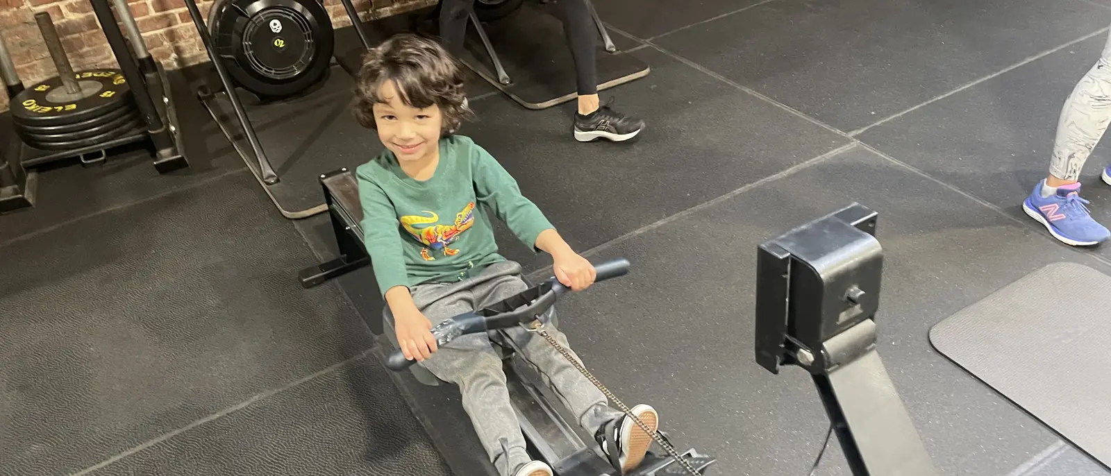 A young HeyKids member grinning while rowing on a Concept2 erg at Heyday Elite Fitness in San Pedro