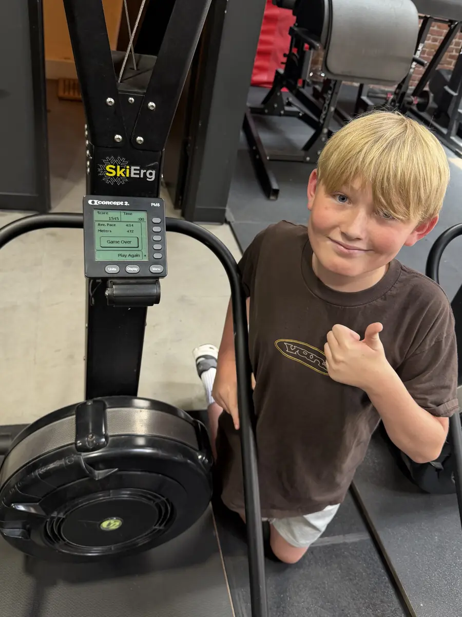A HeyKids student giving a thumbs up next to his SkiErg score after finishing a set